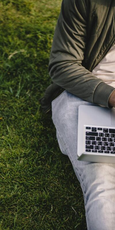 Crop black student with laptop and papers on green lawn